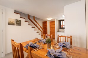 A dining area with a wooden table set for four, a staircase, and a kitchen area in the background.