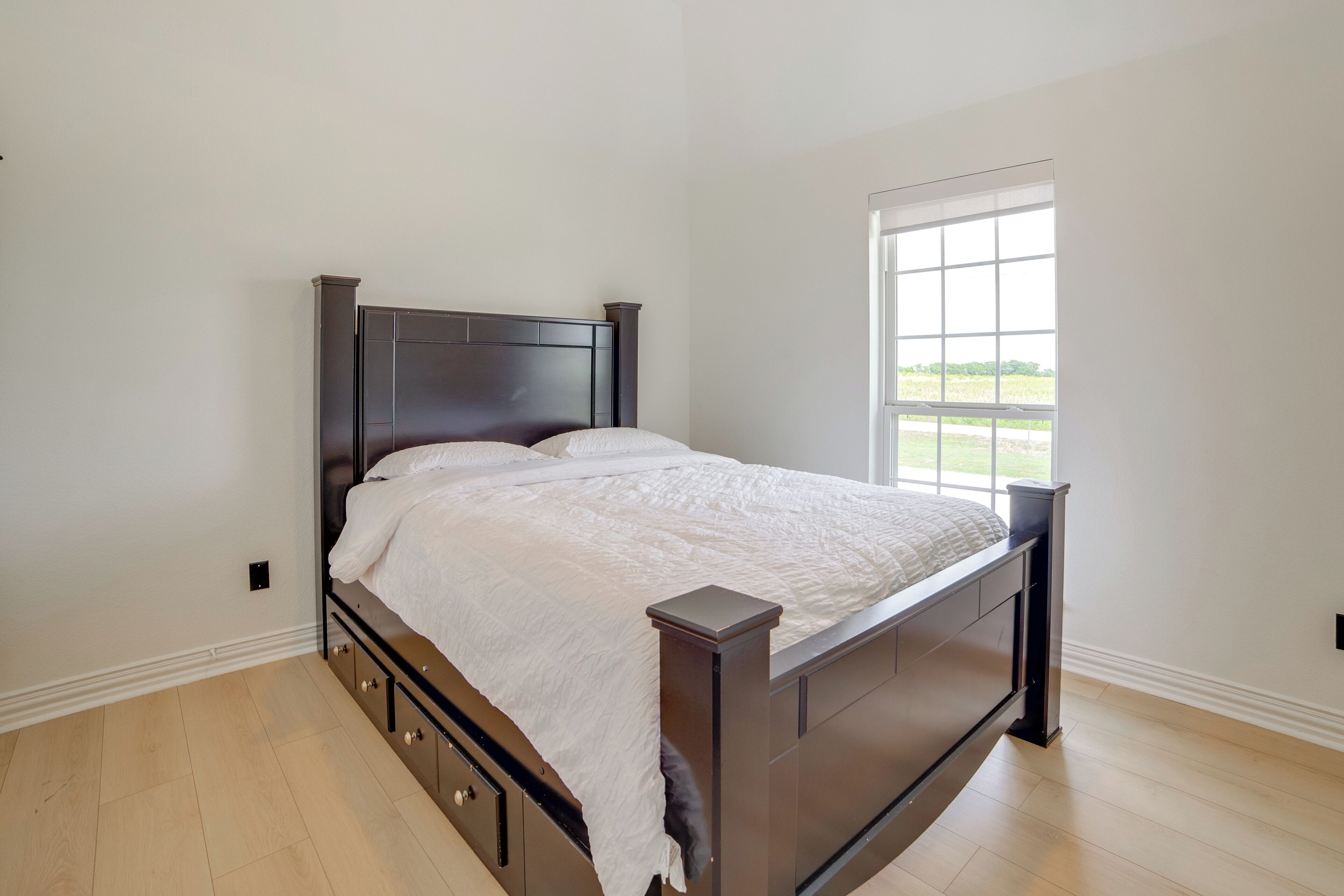A bedroom with a dark wooden bed, white bedding, and a window with a view of greenery.