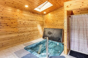 Interior de una cabaña de madera con bañera de hidromasaje de vidrio, tragaluz y zona de ducha.