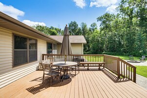 Una terraza de madera con una mesa, sillas, un banco y un área cubierta con un paraguas.