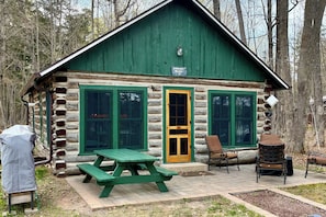 Una cabaña de troncos con techo verde, puerta de madera y una mesa de picnic afuera.