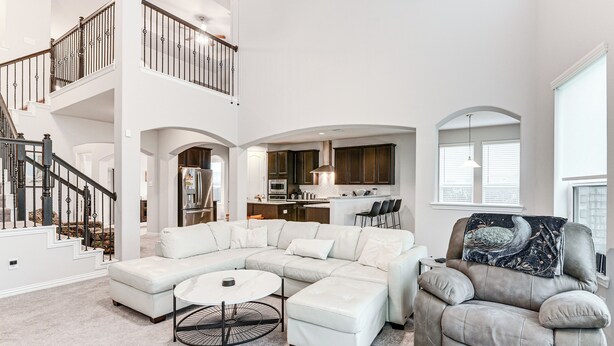 A spacious living area with a sectional sofa, a round coffee table, and a recliner. A staircase with a railing leads to an upper level. - Grand Family Home w/ Patio & Fenced Yard in Arcola (Rosharon)