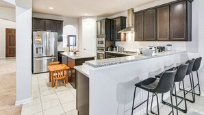 A modern kitchen with dark cabinets, a stainless steel refrigerator, a built-in oven, and a granite countertop. - Grand Family Home w/ Patio & Fenced Yard in Arcola (Rosharon)