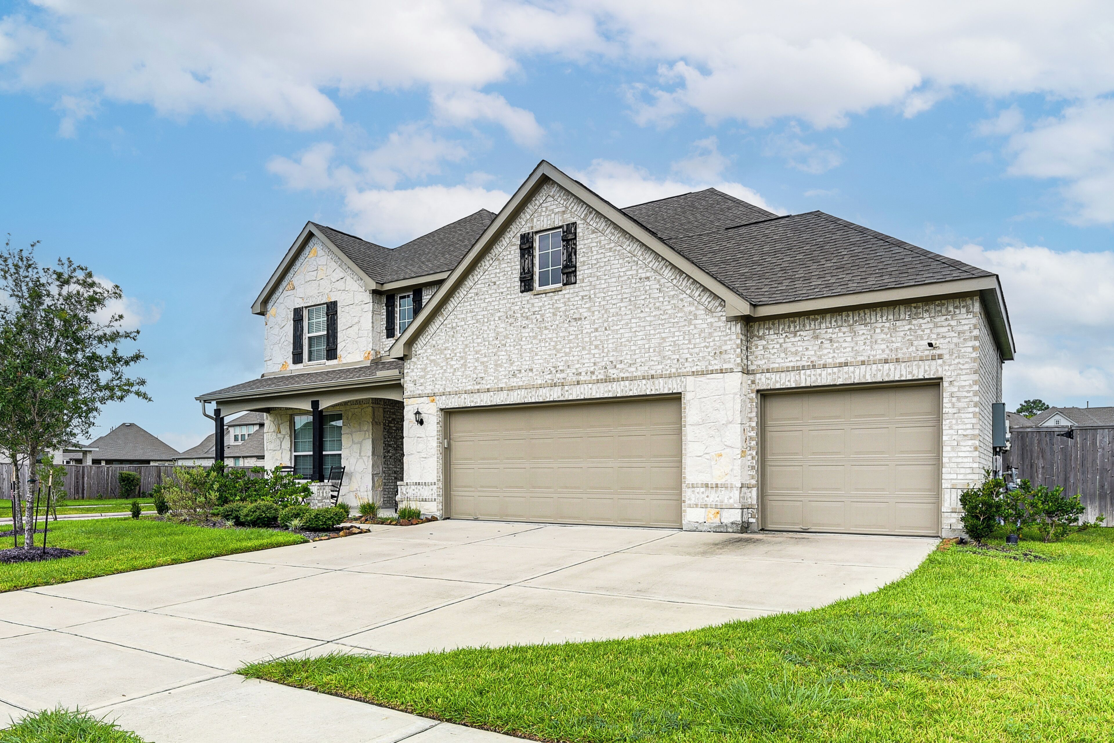 A two-story house with a stone facade, two garage doors, and a well-maintained lawn.