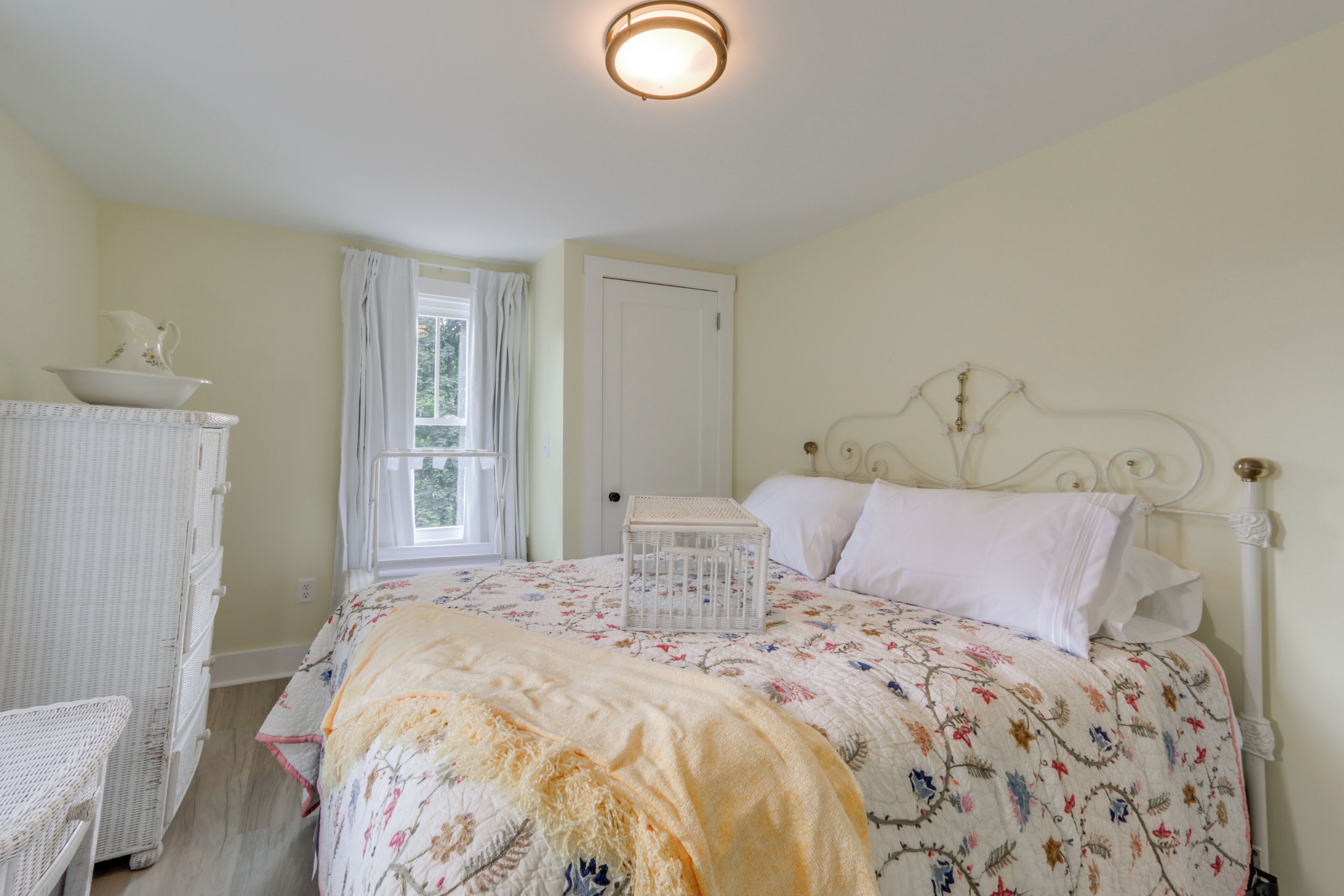 A bedroom with a bed, a dresser, a window with curtains, and a door.