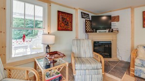 A cozy living room with a fireplace, a television, and a window overlooking a deck. - River Views & Boat Launch Access: Huntingdon Home (Huntingdon)