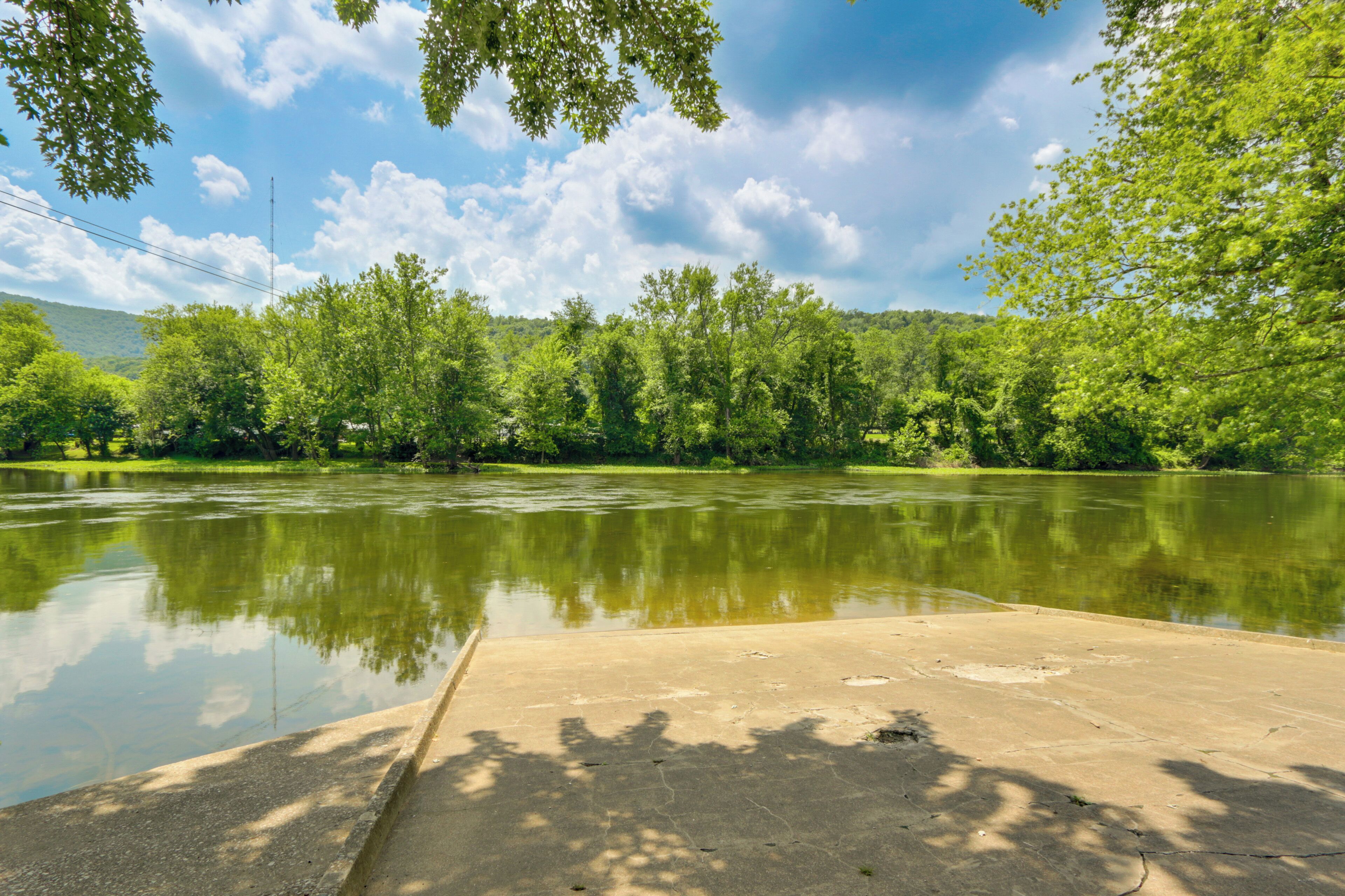 A concrete viewing platform by a calm river with lush greenery and a clear sky.