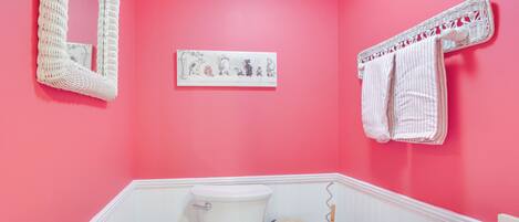 A bathroom with a pink wall, a white toilet, a sink, and a mirror.