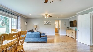 A spacious living room with hardwood flooring, a blue sofa, wooden chairs, a ceiling fan, and a kitchen area with wooden cabinets. - 1 Block to Lake Huron: Pet-friendly Apt w/ Kayaks (Lexington)