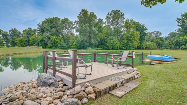 A wooden deck with chairs and a table overlooking a lake, surrounded by rocks and greenery. - 1 Block to Lake Huron: Pet-friendly Apt w/ Kayaks (Lexington)