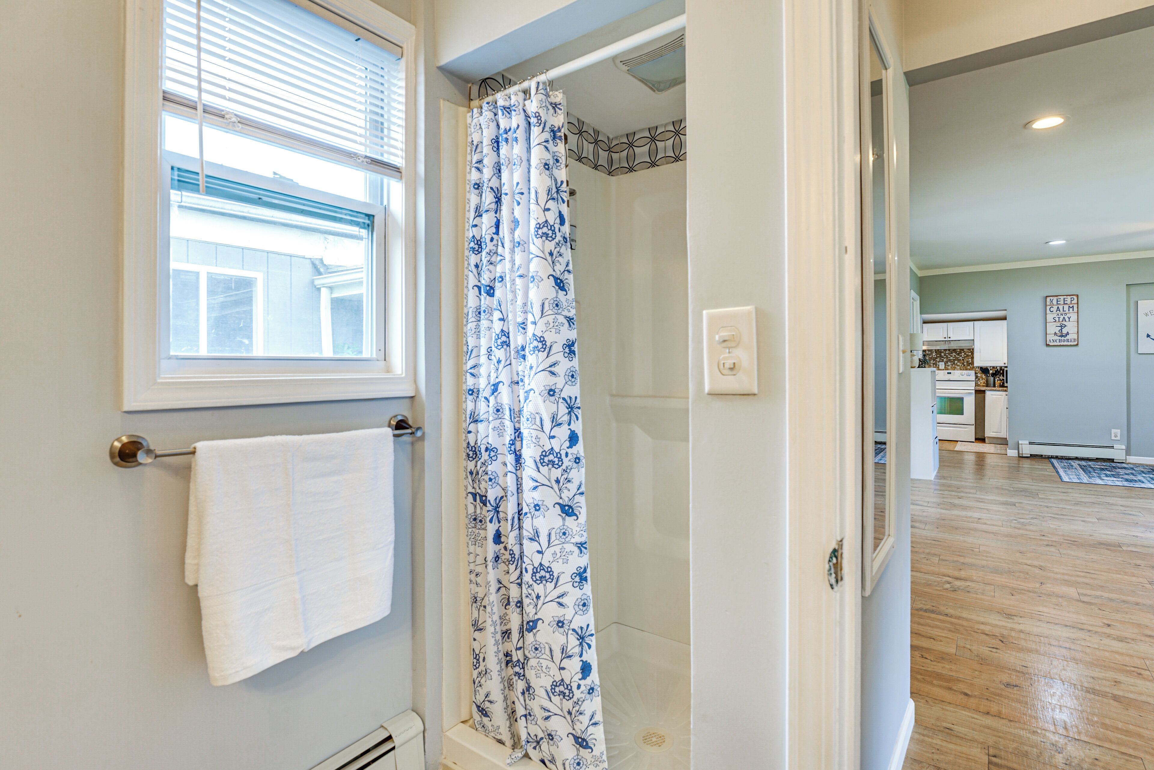 Une salle de bain avec une douche, un porte-serviettes et une fenêtre avec des stores.