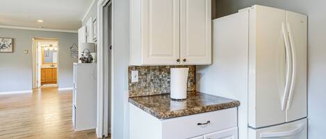 A kitchen with white cabinets, a granite countertop, and a white refrigerator.