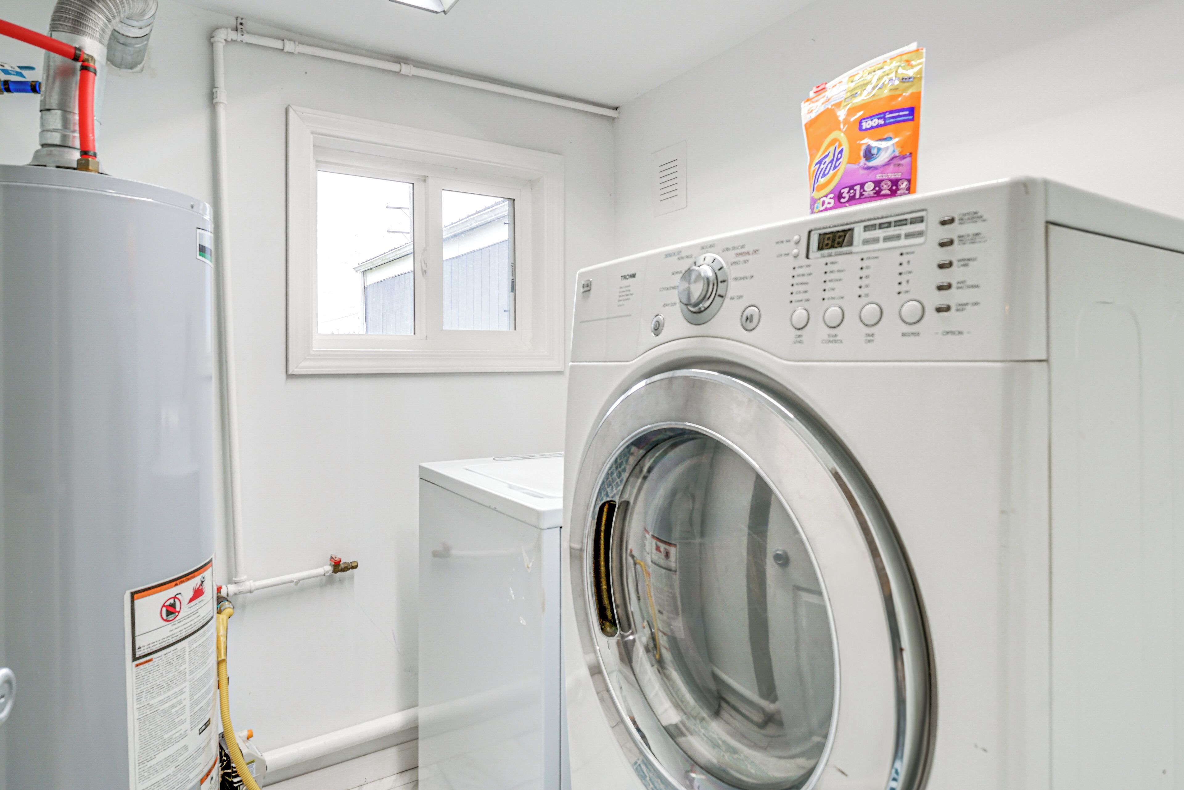 A laundry room with a front-loading washing machine, a water heater, and a window.