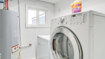 A laundry room with a front-loading washing machine, a water heater, and a window.