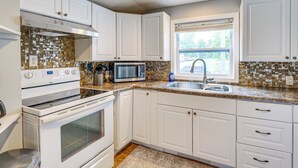 A kitchen with white cabinets, a microwave, stove, and a window with blinds. - 1 Block to Lake Huron: Pet-friendly Apt w/ Kayaks (Lexington)