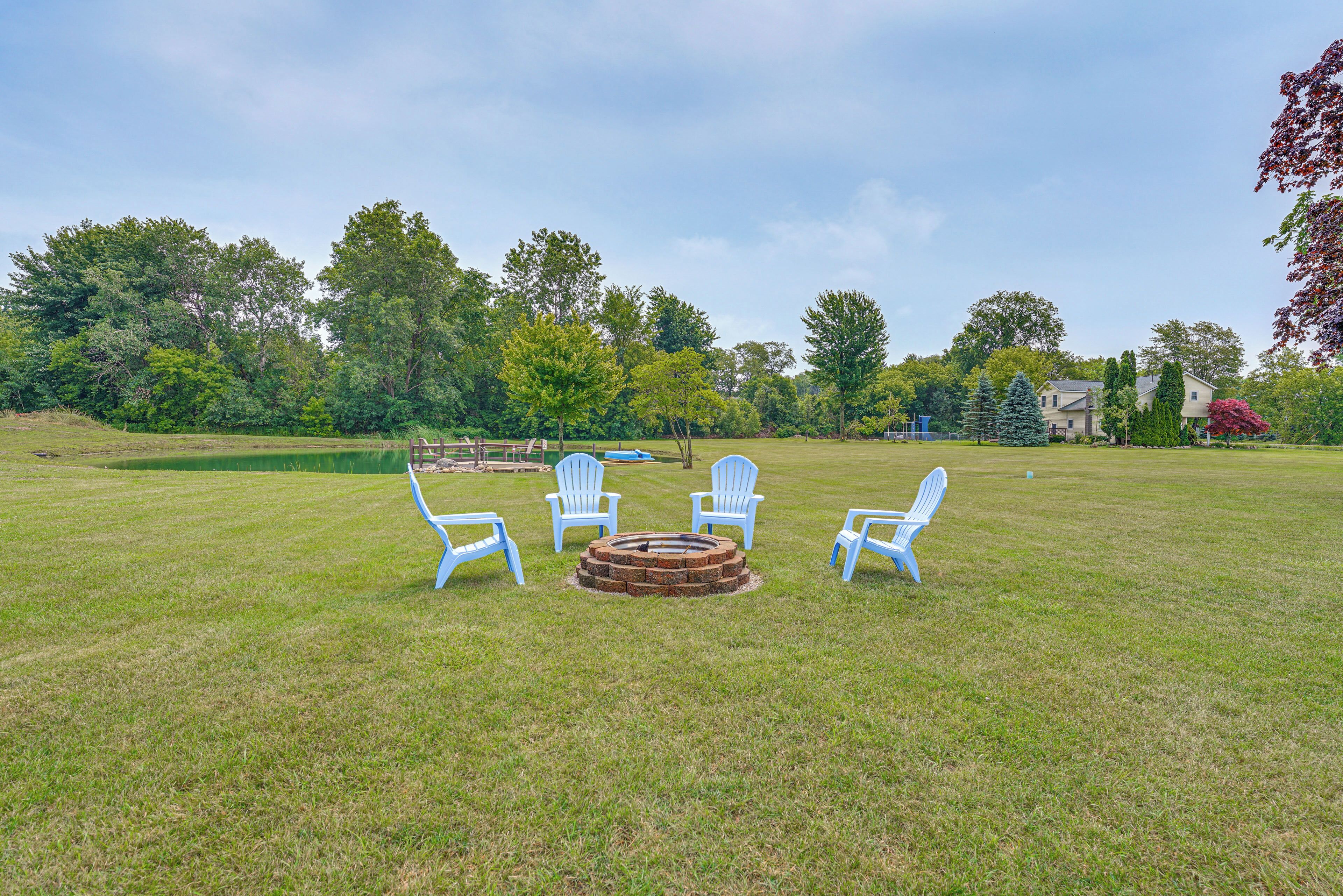 A grassy outdoor area with a circular fire pit and four blue chairs arranged around it.