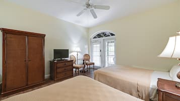 A hotel room with two beds, a wooden wardrobe, a desk with a lamp, a television, and a ceiling fan.