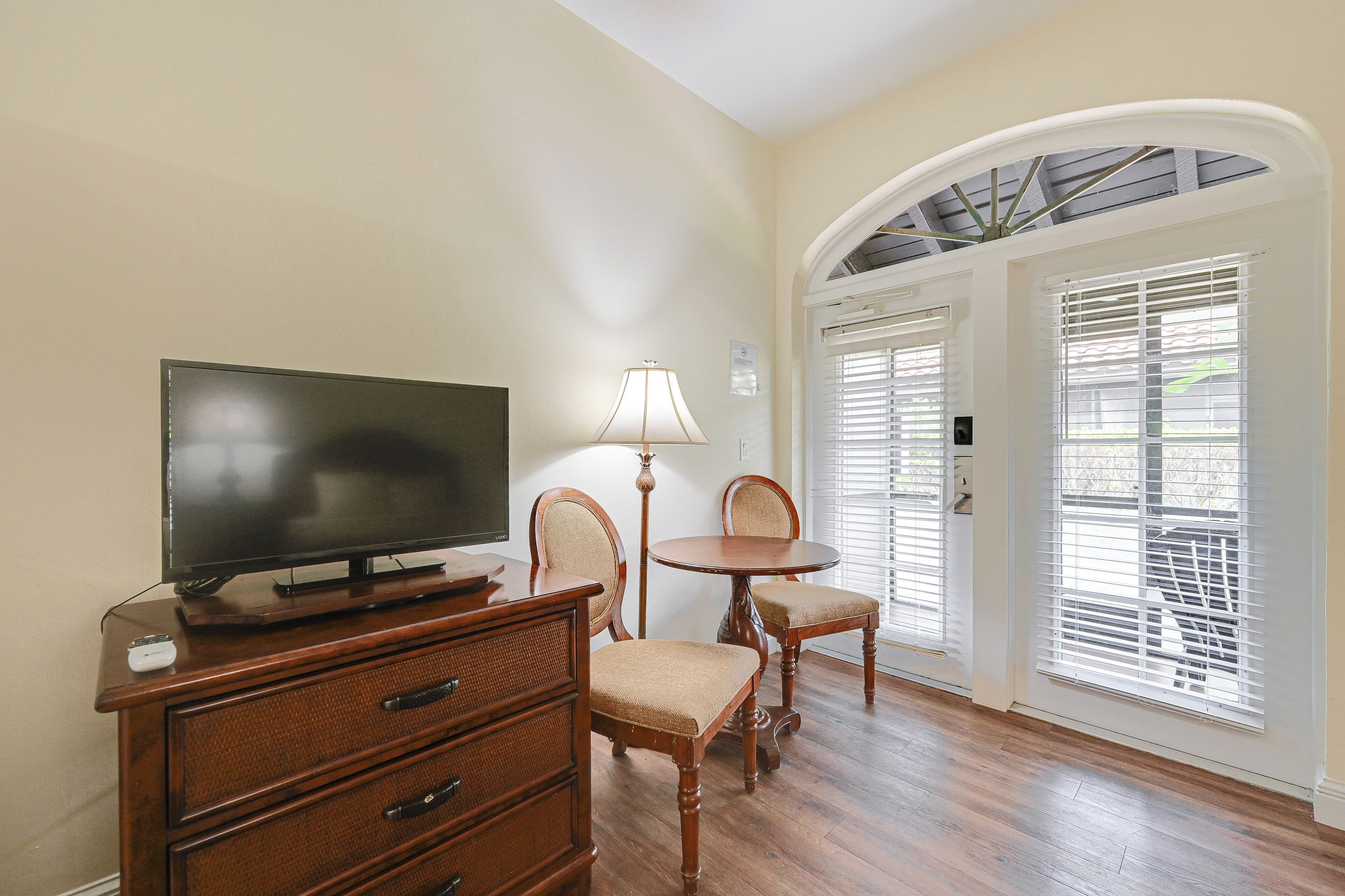 A living room with a television, wooden furniture, and a dining area with a lamp.