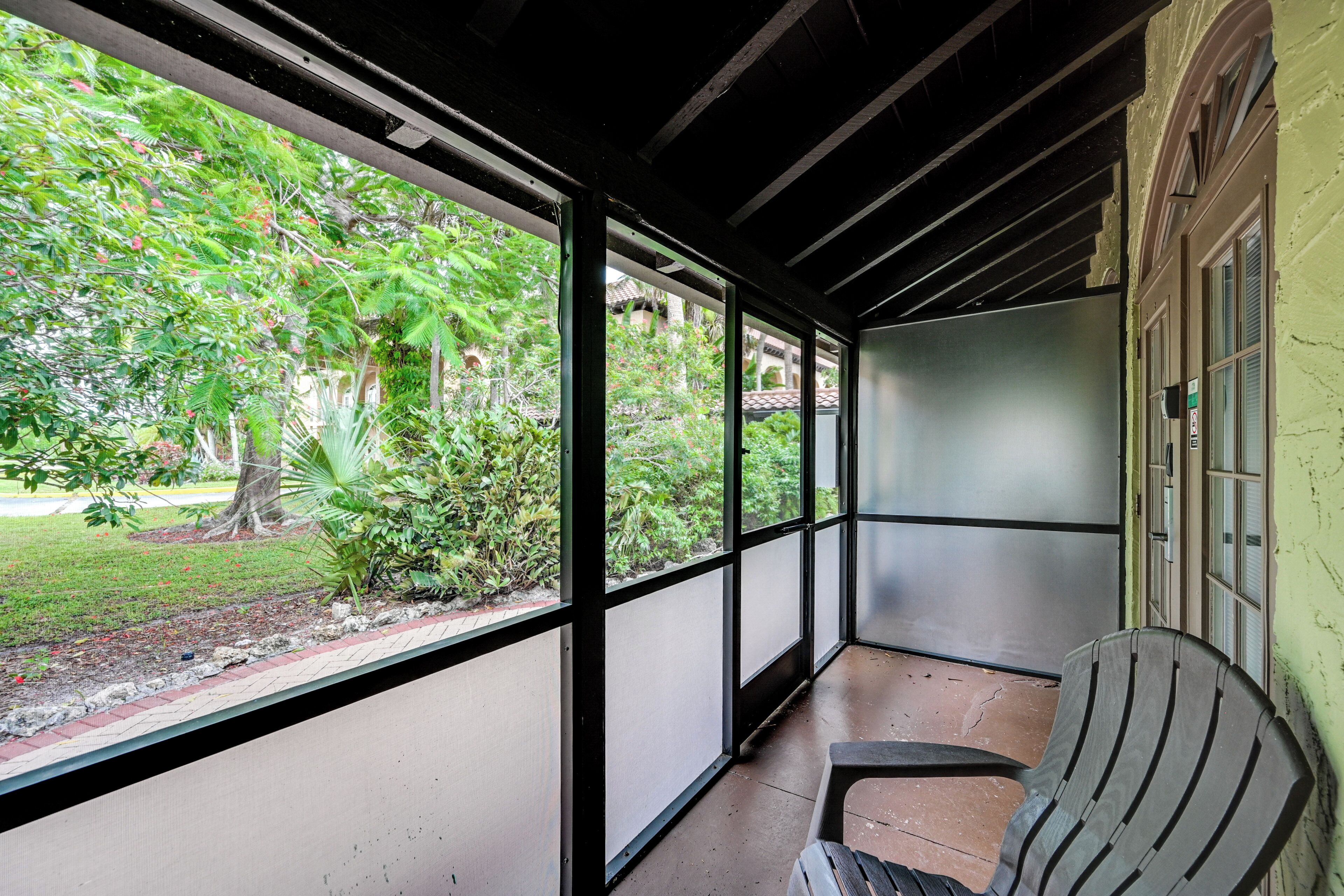 Uma área externa coberta com vista para vegetação, uma cadeira e um edifício com parede verde e janelas.