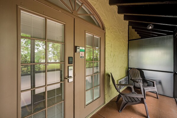 A room with a large window, a door with a keypad lock, and a chair near the window.