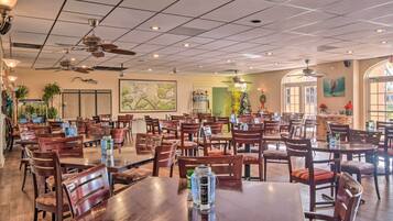 A spacious restaurant with multiple tables and chairs, ceiling fans, and large windows.