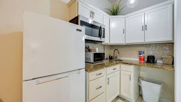 A kitchen with white cabinets, a stainless steel refrigerator, a microwave, and a sink.