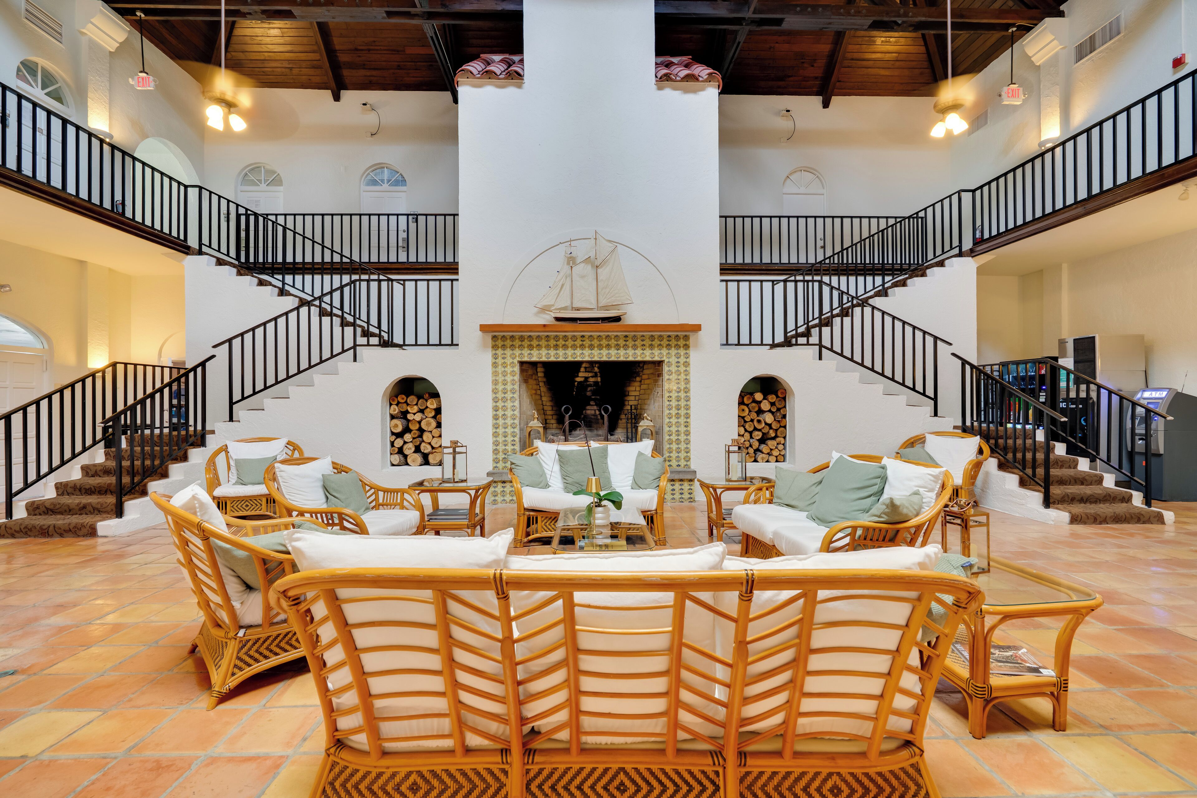A spacious living area with wicker furniture, a fireplace, and a grand staircase.