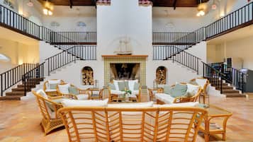 A spacious living area with wicker furniture, a fireplace, and a grand staircase.