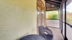 Un espacio al aire libre techado con una mesa y sillas de patio, una puerta con paneles de vidrio y vistas a la vegetación.