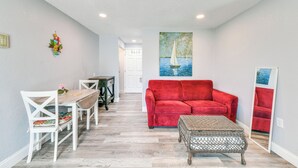 Un salon avec un canapé rouge, des fauteuils blancs, une table en bois et un pouf en osier.