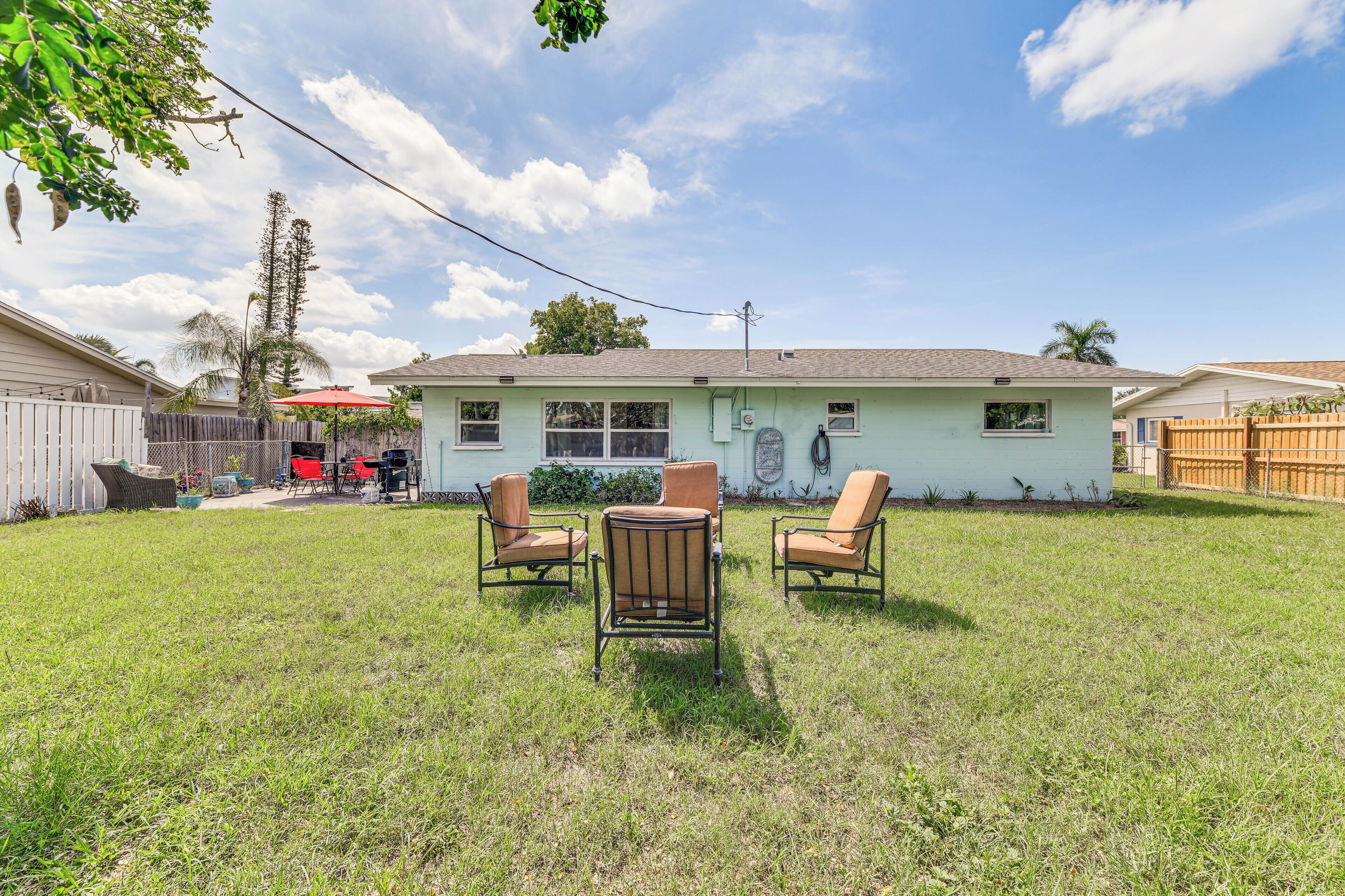 A house with a backyard featuring a lawn, a patio with two chairs, and a small table.
