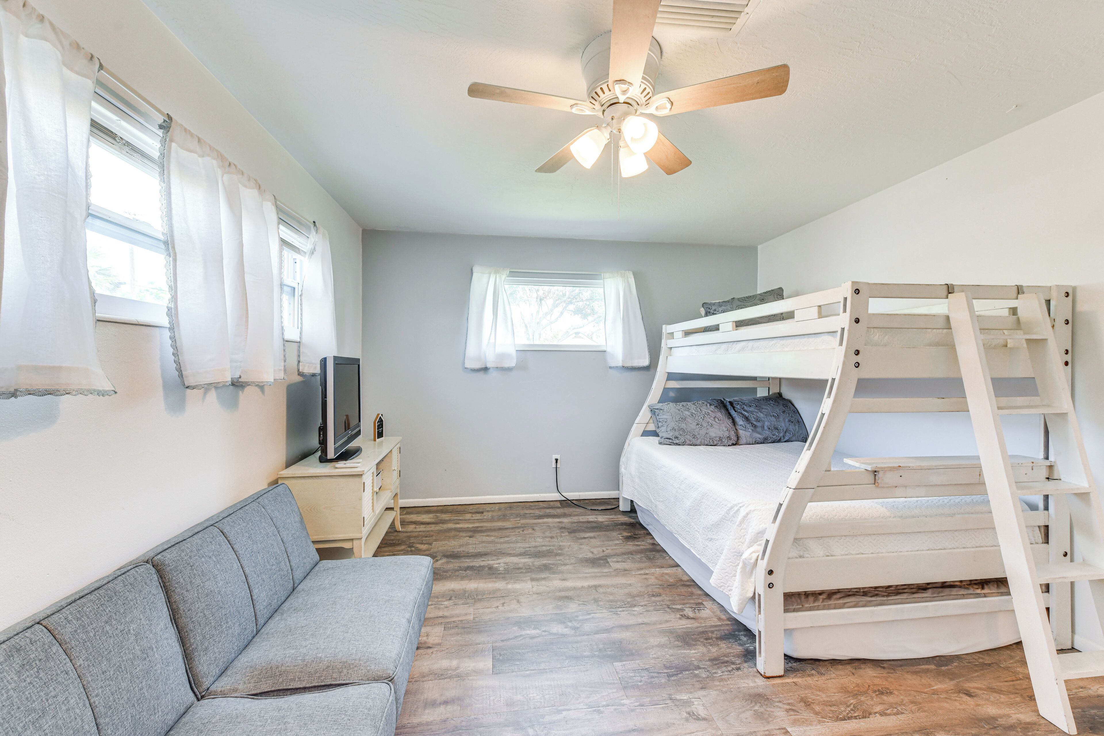 A bedroom with a bunk bed, a sofa, a television on a nightstand, and a ceiling fan.