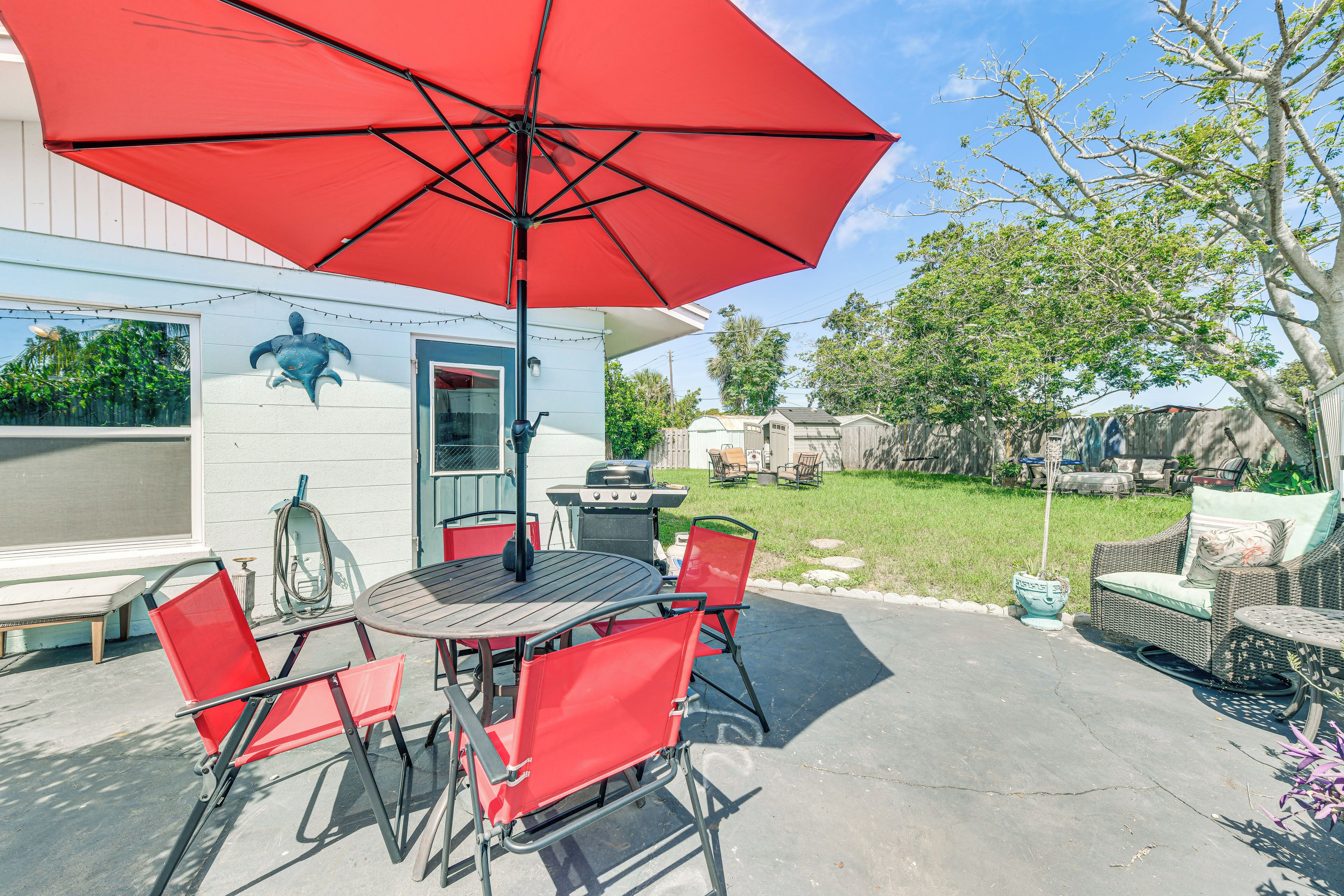 An outdoor patio with a round table, red chairs, and a red umbrella.