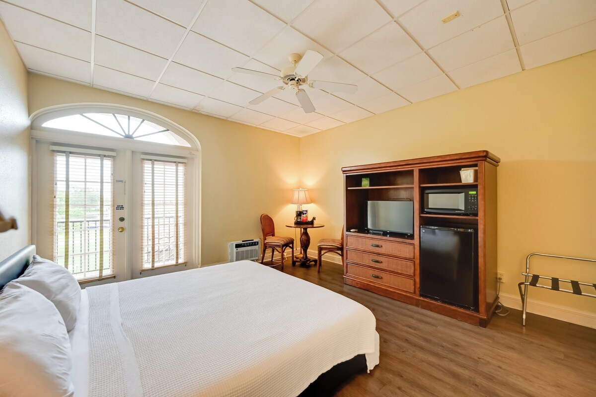 A hotel room with a bed, a desk, a chair, a television, a microwave, and a refrigerator.
