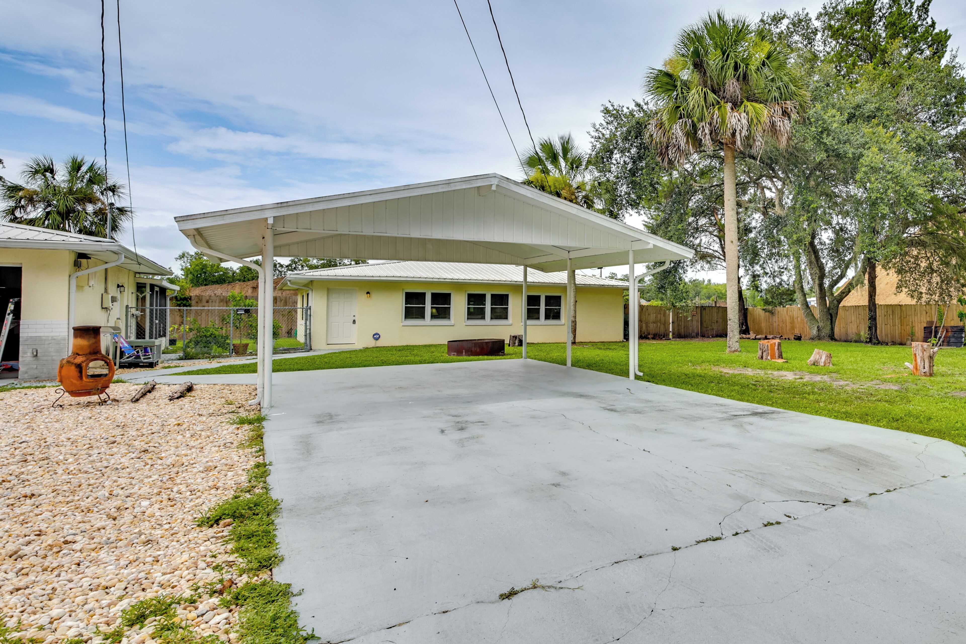 A covered patio area with a concrete floor, a small outdoor kitchen, and a lawn with trees and a wooden fence.