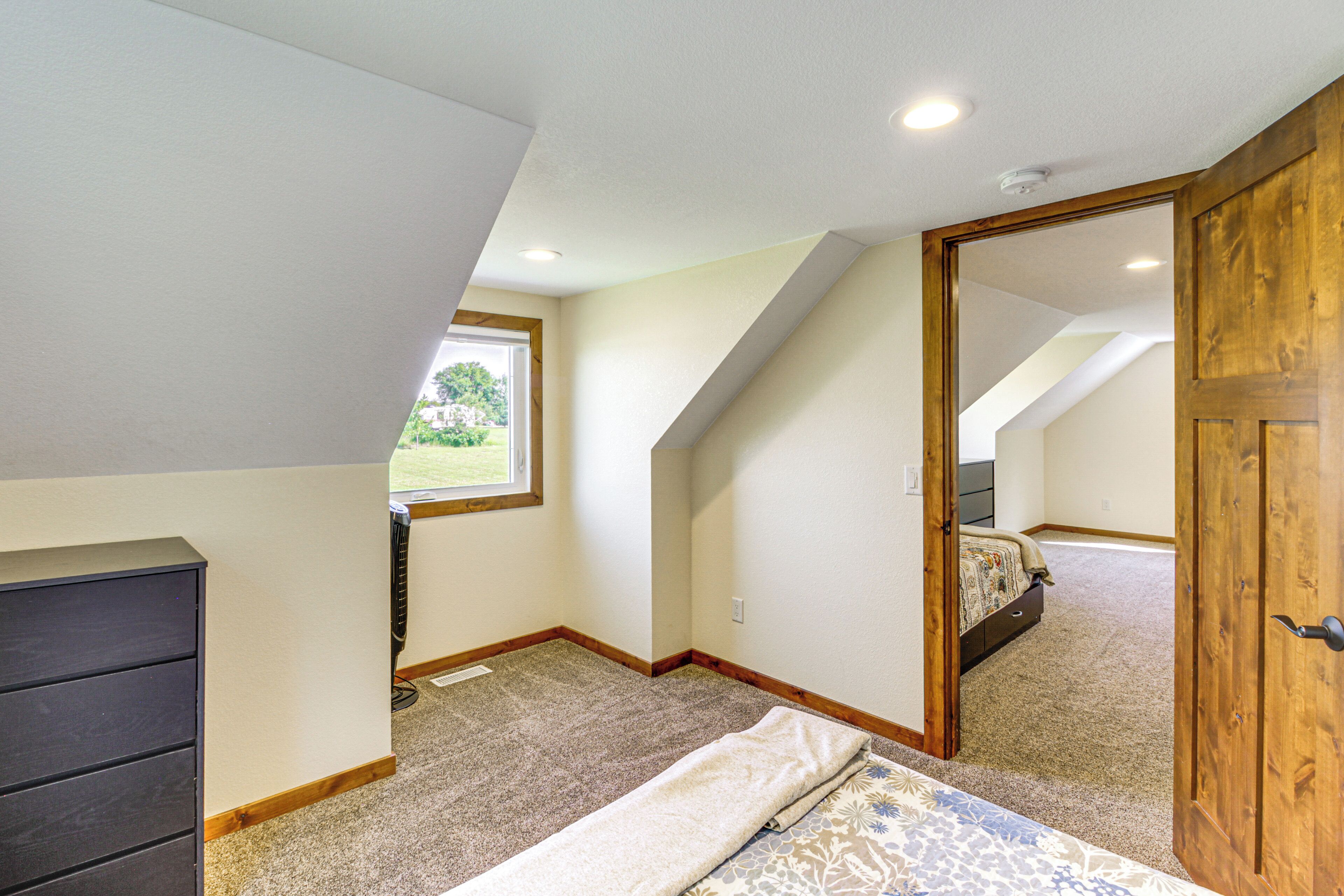 Un dormitorio con techo inclinado, ventana, cama, cómoda y puerta.