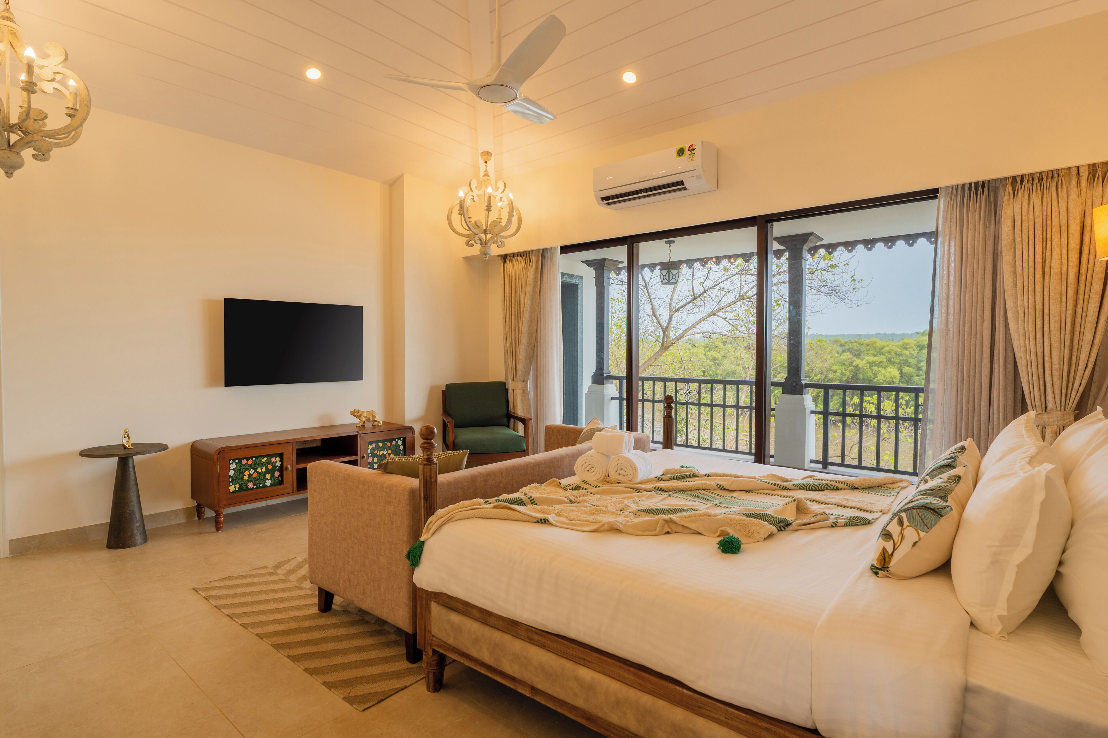 A bedroom with a large bed, a TV, a chandelier, an air conditioner, and a balcony with a view.