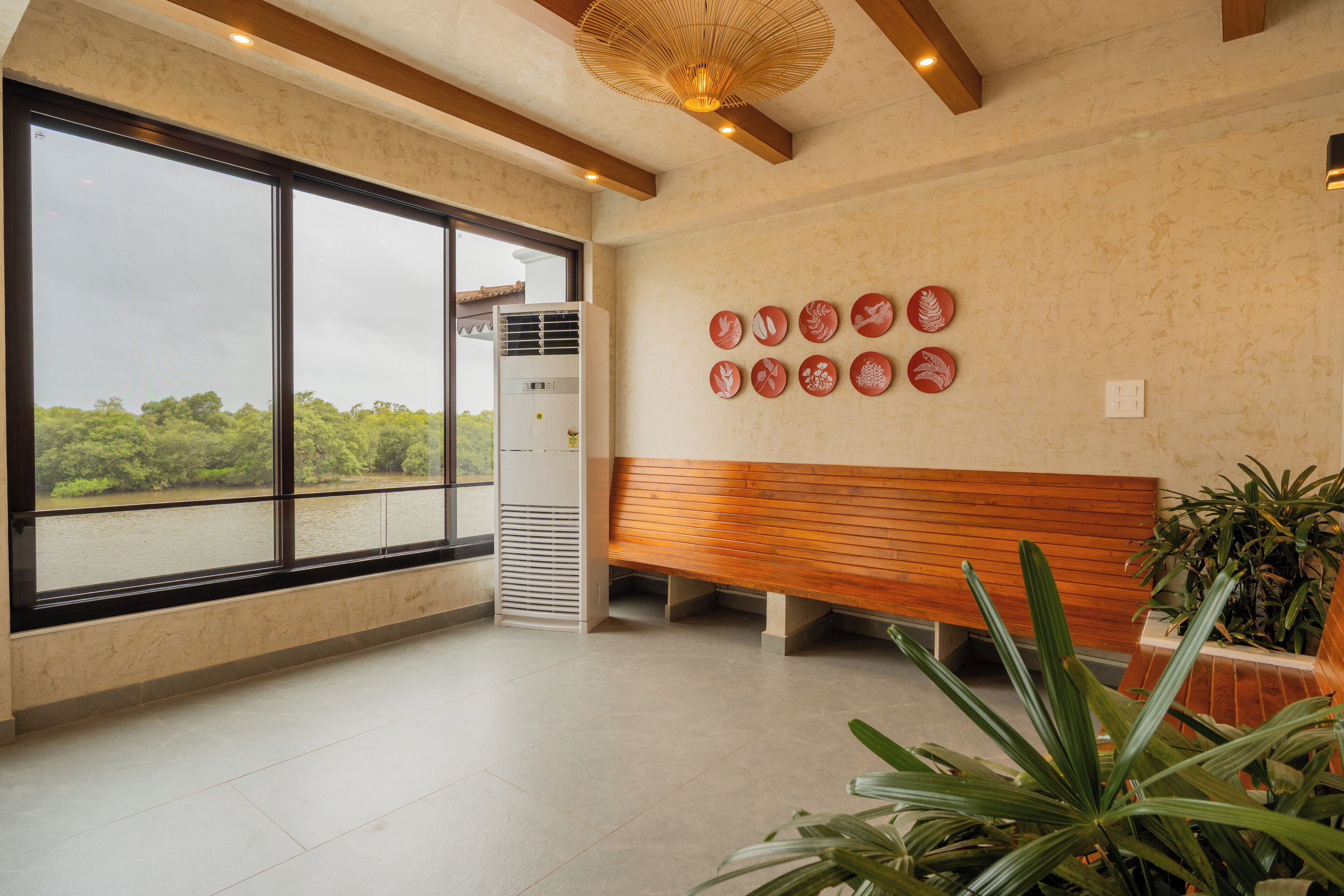 A spacious room with large windows, a wooden bench, and a wall decorated with circular plates.