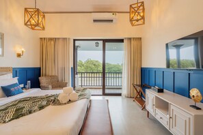 Habitación de hotel con cama, escritorio, silla, ventana grande con vistas a zonas verdes y balcón.