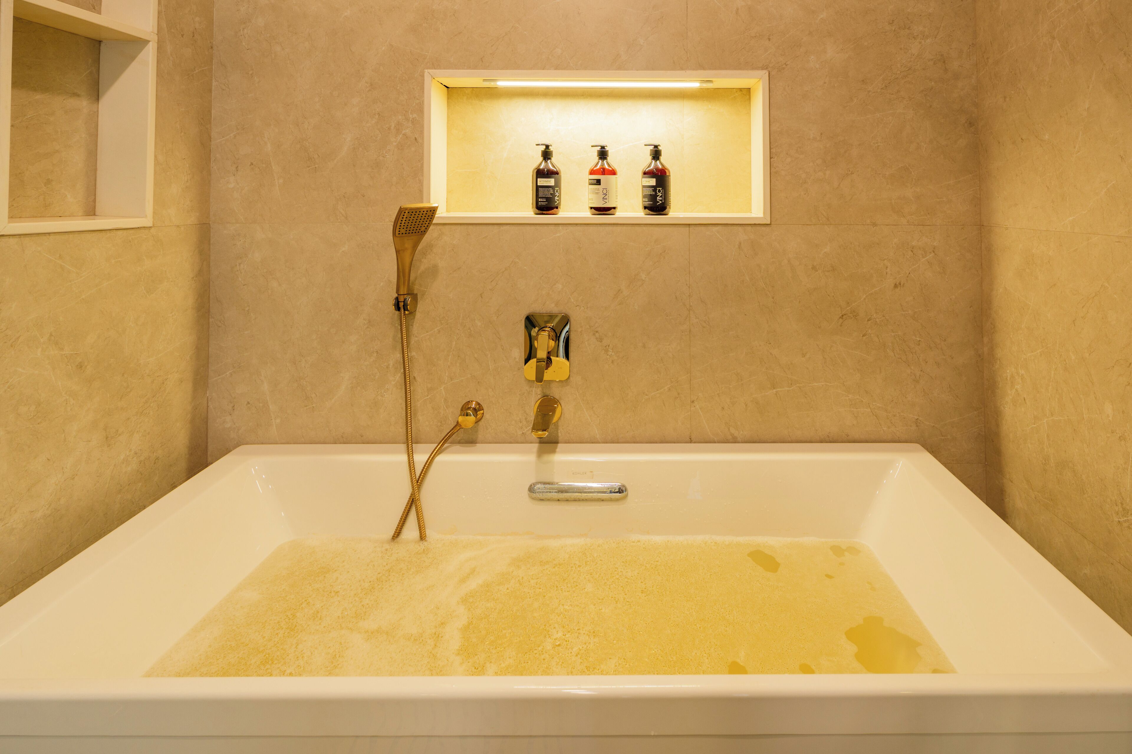 A bathtub with a showerhead, a shelf with three bottles, and a mirror on the wall.