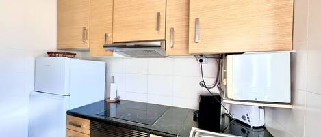 A compact kitchen with wooden cabinets, a built-in oven, a microwave, and a stainless steel sink.
