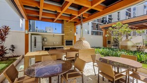 Un patio al aire libre con mobiliario de mimbre, un horno de ladrillo y vistas de los edificios circundantes.