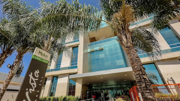 Un hotel moderno con fachada de vidrio, palmeras y un cartel que indica 'Long Stay'.