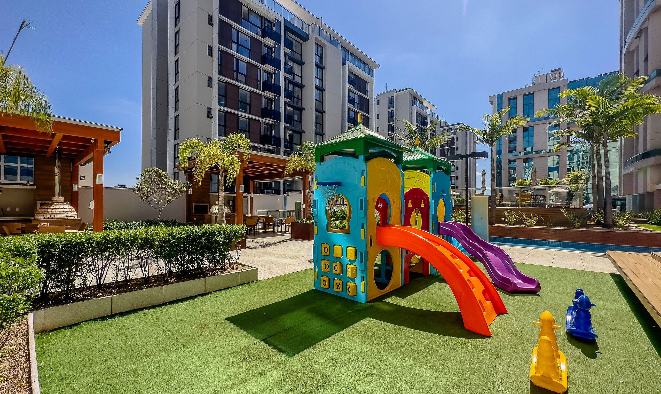 A children's play area with a slide, surrounded by greenery and modern buildings.