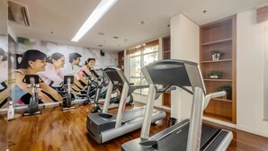 Un gimnasio con cintas de correr y bicicletas estáticas, suelo de madera y un ventanal que proporciona luz natural.