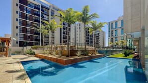 Un hotel moderno con piscina, mobiliario exterior y un jardín bien cuidado.