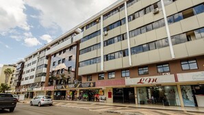A multi-story building with various shops on the ground floor, including a pizzeria and a salon. - Apto 1Q 350m do PQ. Bosque do Sudoeste - SVS0219 (Sudoeste e Octogonal)