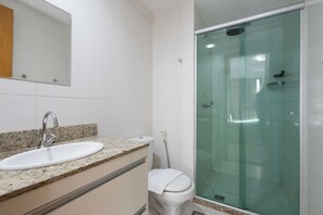 A bathroom with a granite countertop sink, a white toilet, and a glass-enclosed shower. - Studio em cond. c/ Academia, Asa Norte SMZ407 (Brasília)