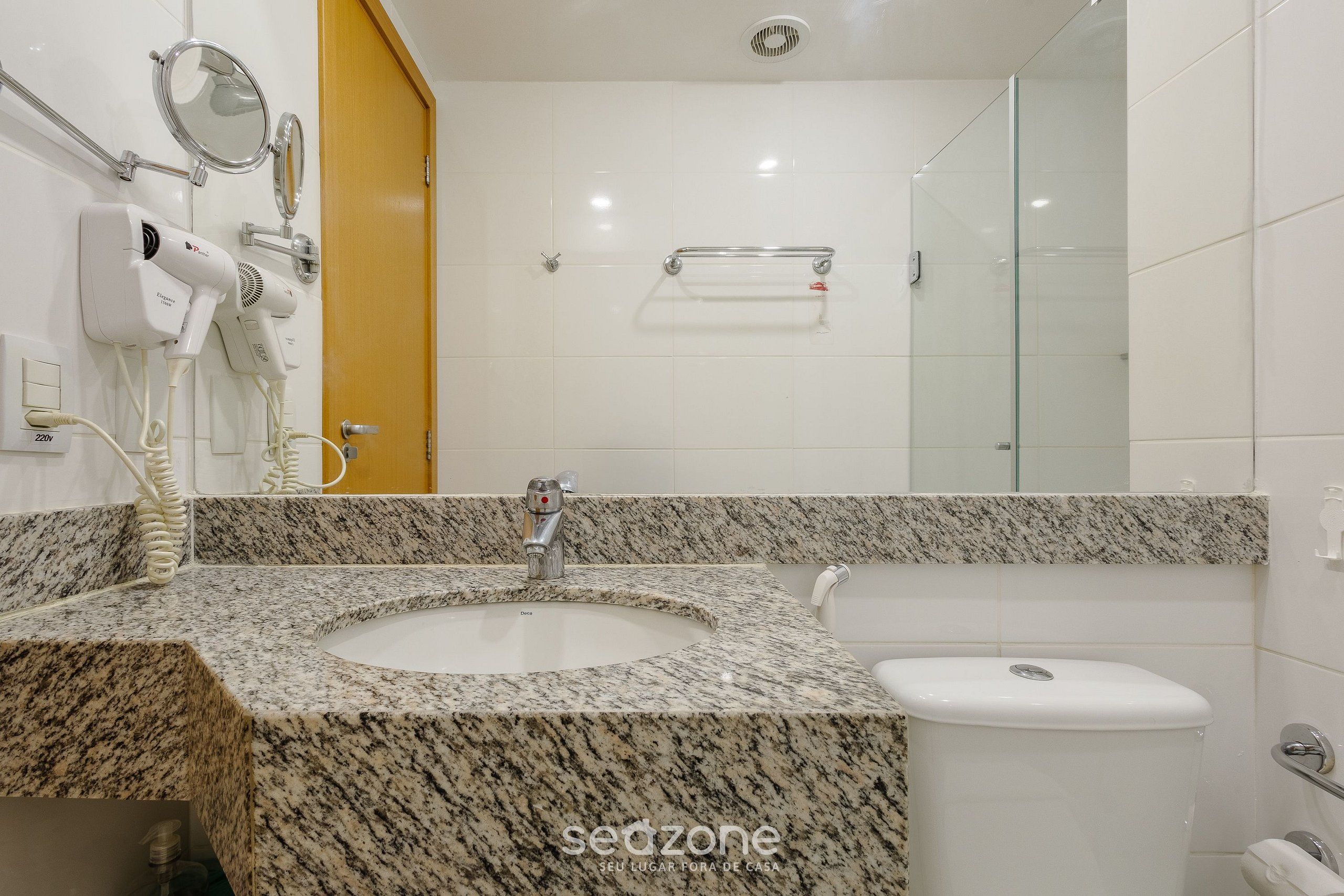 Ein Badezimmer mit Granitwaschtisch, Waschbecken, Toilette und einer Duschkabine aus Glas.
