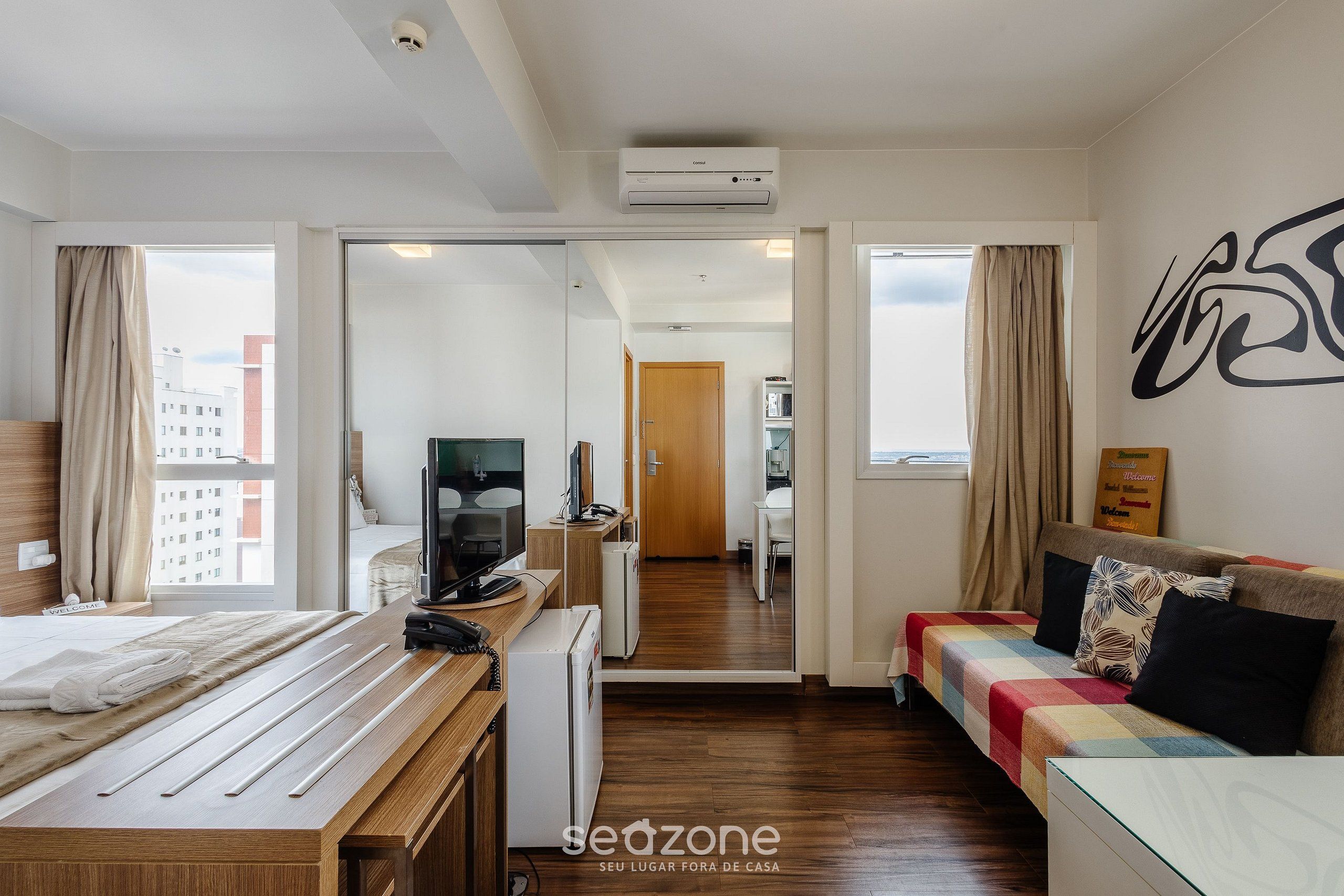 Una habitación de hotel moderna con una cama de madera, un sofá, un escritorio y vistas a la ciudad.